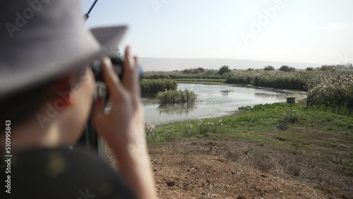Young birdwatcher is observing natural habitat with binoculars from far away. Female woman looking at plants and birds from observation post or station in nature reserve or park. Enthusiastic birder