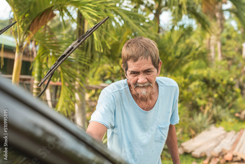 An old man washes his black hatchback. A car owner cleaning and taking care of his auto early in the morning.