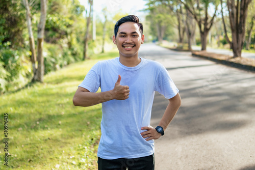Cheerful young Asian man showing thumbs up gesture in the nature. Healthy lifestyle © Sewupari Studio