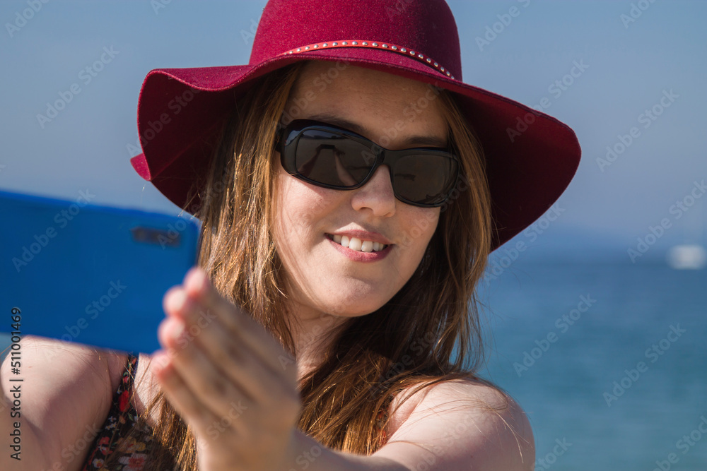 young smiling woman making a selfie or live video on the beach with mobile phone