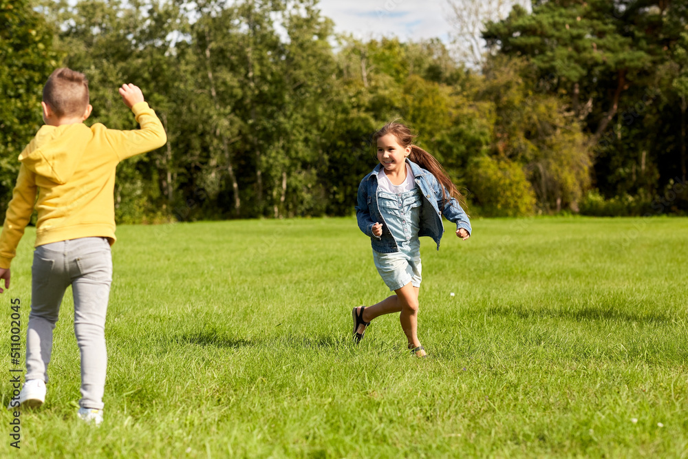 childhood, leisure and people concept - happy children playing tag game and running at park