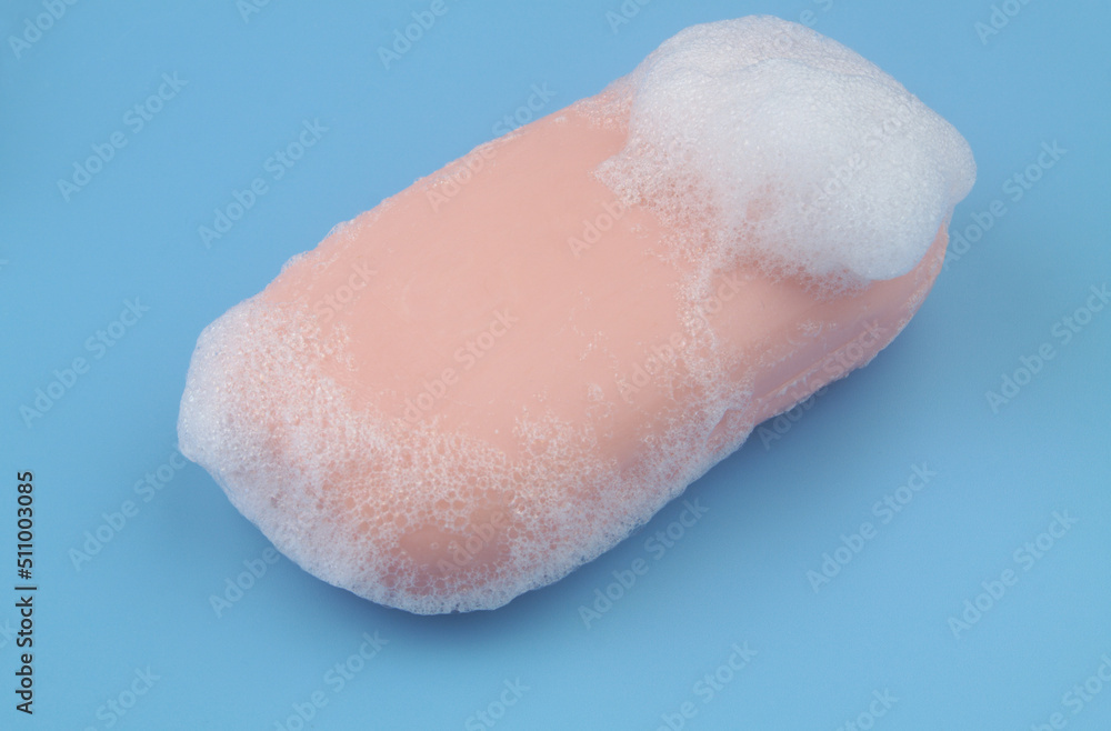 Fototapeta premium Pink soap with white foam bubbles on blue background. 
