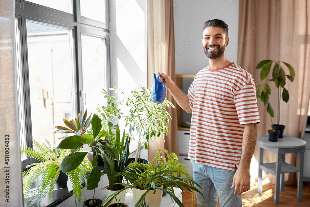 people, nature and plants care concept - happy smiling man watering flowers at home people, nature and plants care concept - happy smiling man watering flowers at home