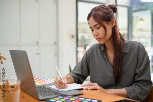 Focused young asian female graphic designer sketching her design on blank notebook