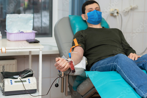 bone marrow donation. man in medical mask, male hand holding red ball, blood transfusion system, blood bag. soft focus