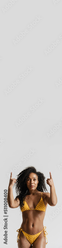 Naklejka premium Black woman in swimsuit smiling and pointing fingers upward