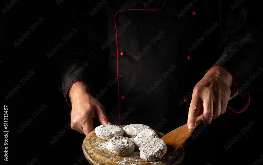 Meat cutlets in flour on a cutting board in the hands of a chef. Free space for advertising on a black background
