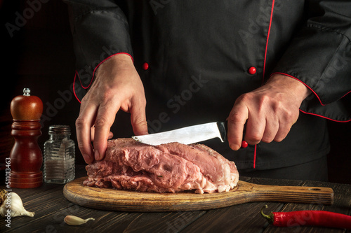 Chef cutting raw meat with a knife before grilling in the kitchen. Hotel menu or recipe idea