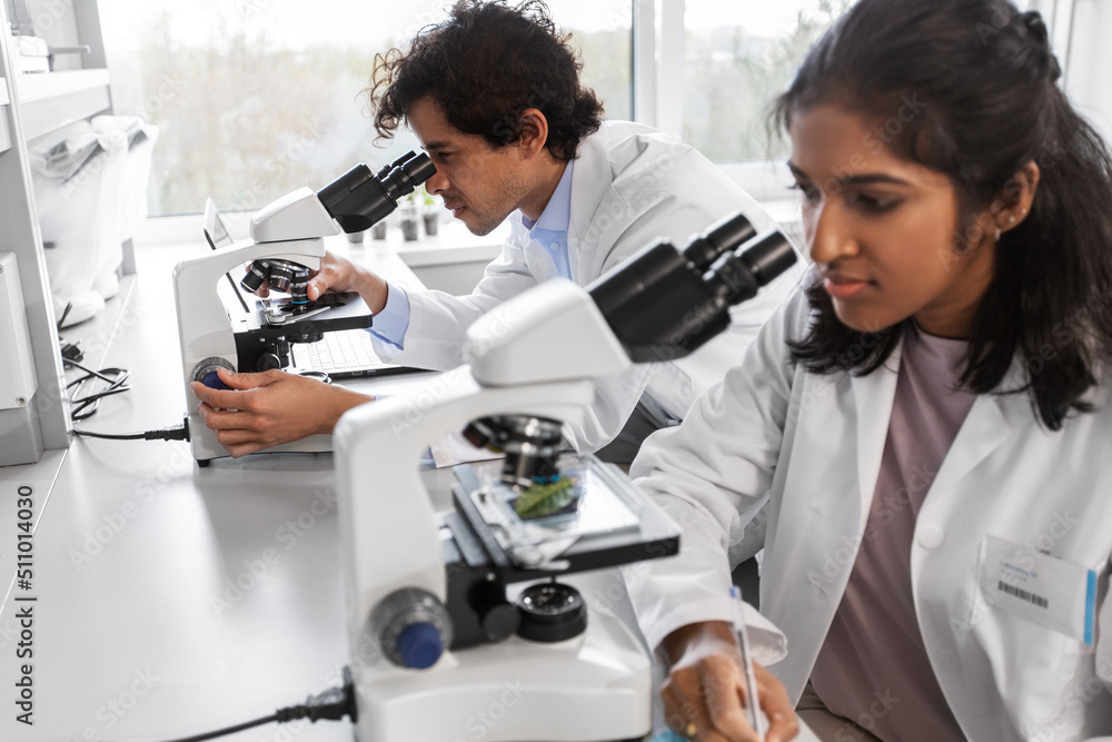 science research, work and people concept - international team of scientists with microscopes working in laboratory science research, work and people concept - international team of scientists with microscopes working in laboratory