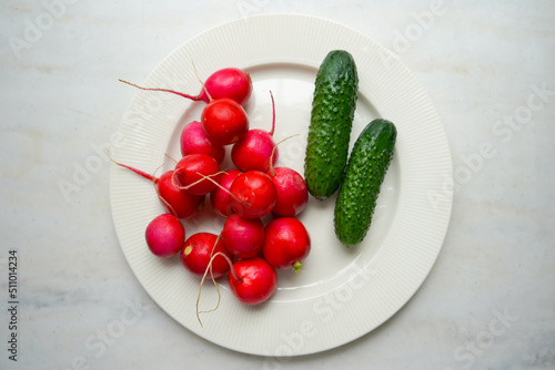 Spring fresh vegetables radishes, cucumber and greens on white plate. Fresh organic farm vegetables, radishes, cucumbers.