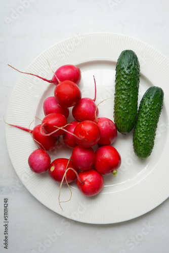 Spring fresh vegetables radishes, cucumber and greens on white plate. Fresh organic farm vegetables, radishes, cucumbers.