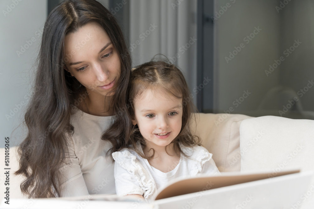Mom and daughter are reading a book on the sofa. Study and activities with children at home, mental development, free time with children Mom and daughter are reading a book on the sofa. Study and activities with children at home, mental development, free time with children