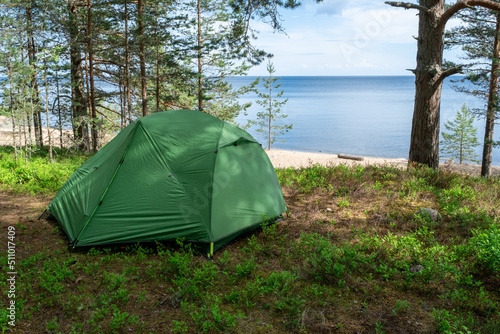 A tent for hiking on the lake shore on a summer day. Hiking along the sea with tourist equipment.