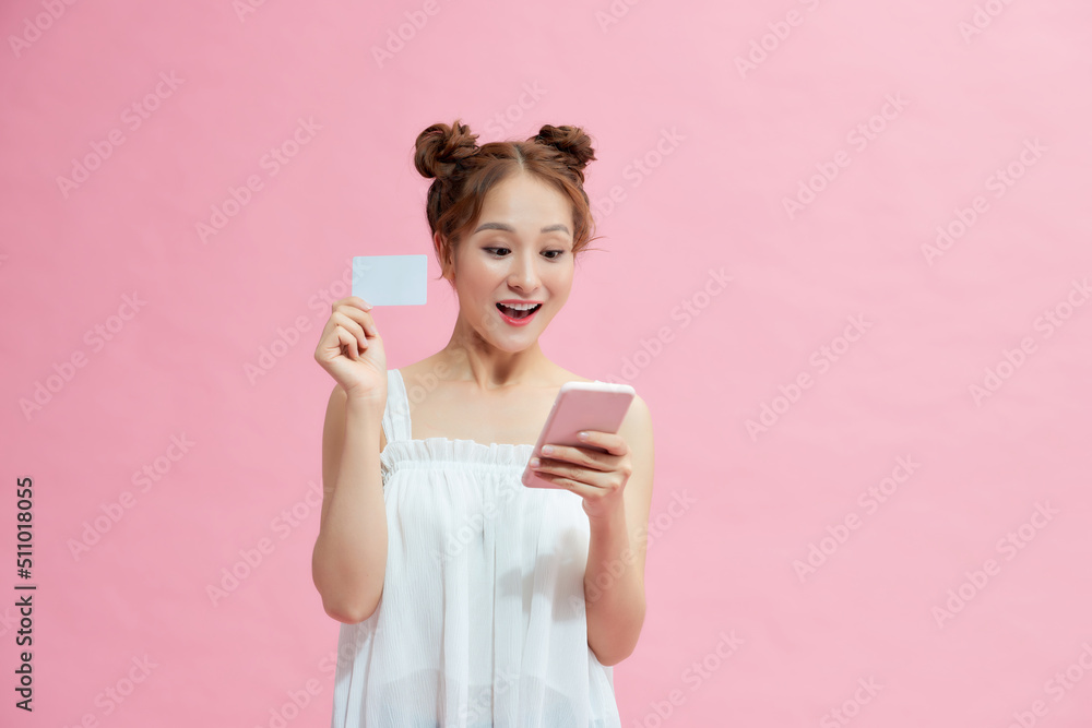 Portrait of a smiling woman holding credit card and mobile phone over pink background Portrait of a smiling woman holding credit card and mobile phone over pink background