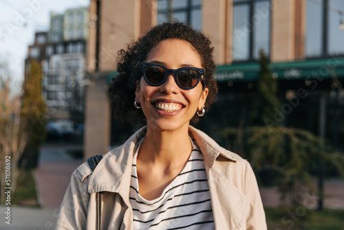 Close up happy young african woman smiling with teeth spending time outdoors. Curly brunette wears sunglasses in sunny weather. Lifestyle, different emotions, leisure concept.