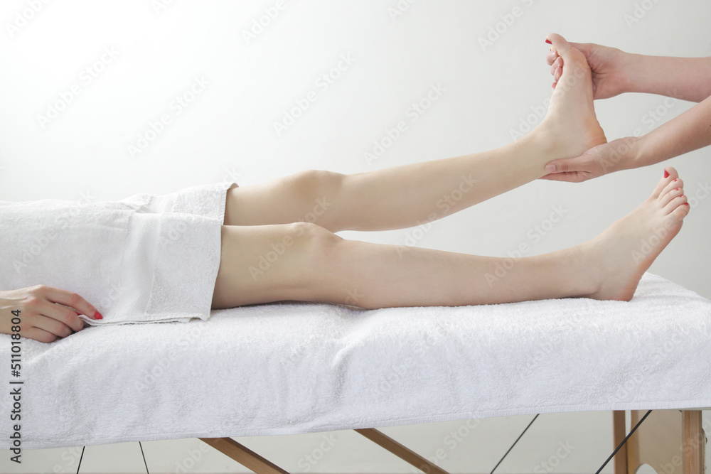 Fototapeta premium Feet massage. Young Caucasian woman enjoing soft shooting partial relax massage experience at spa salon.
