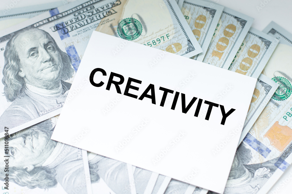 Naklejka premium Creativity text on a card against the background of dollar bills on the table