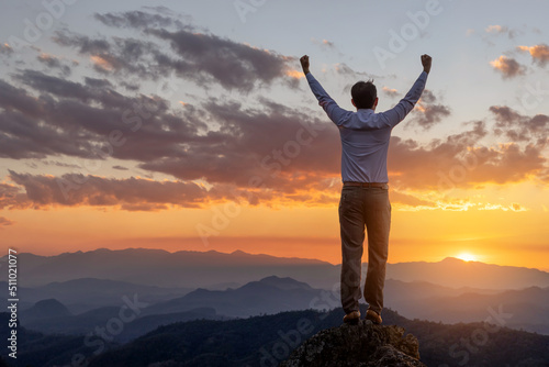 Success concept.Male business standing on top rock with his hands raised enjoy sunny day