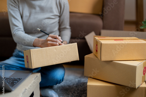 Shipping shopping online, young start up small business owner writing address on cardboard box at workplace.small business entrepreneur SME or freelance asian woman working at home