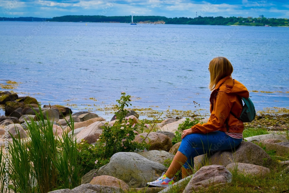 Frau mit Rucksack sitzt am Ufer, Kieler Förde, Ostsee