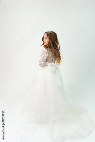 A little girl with a beautiful hairstyle and white dress is looking to the side