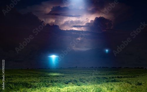 Scenic sci-fi image: UFO or alien spacecraft inspect green grass field with bright spotlight in dark stormy night sky