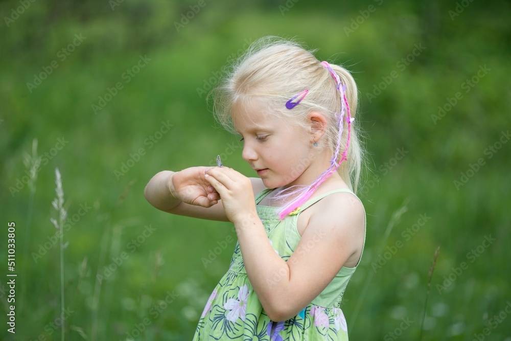 A little girl looks at a butterfly on her hand in the summer meadow A little girl looks at a butterfly on her hand in the summer meadow