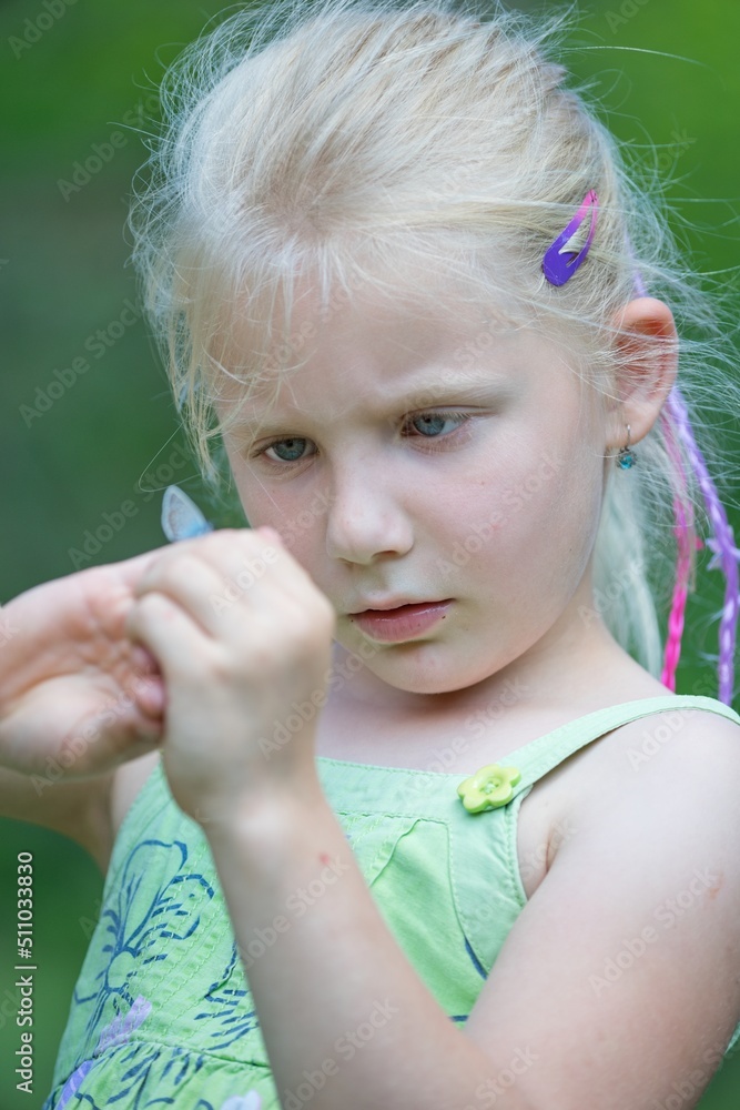 A little girl looks at a butterfly on her hand in the summer meadow A little girl looks at a butterfly on her hand in the summer meadow
