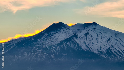 Watching beautiful sunset behind volcano Mount Etna near Castelmola, Taormina, Sicily, Italy, Europe, EU. Clouds with vibrant red orange color. Scenic view on snow capped mountain peak during twilight