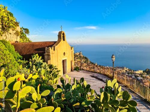 Chiesa di San Biagio of Castelmola with panoramic view on coastline of Ionian Mediterranean sea near Taormina, Sicily, Italy, Europe, EU. A field of cactus around the church at sunset golden hour time photo