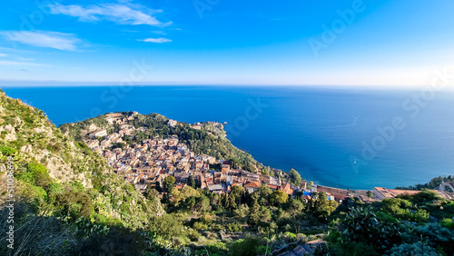Panoramic aerial view on sunny day on coastline of Ionian Mediterranean sea, Taormina, Sicily, Italy, Europe, EU. Saracen castle on the hills of tourist town Taormina. Vibrant blear blue sky