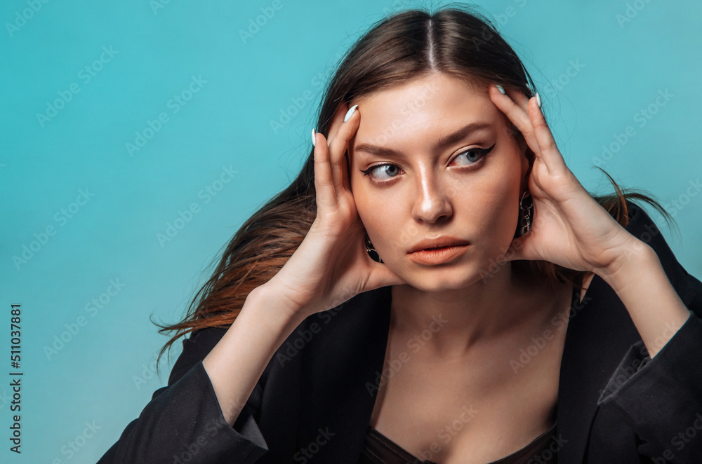 Obraz premium young woman massages her face with her hands on a turquoise background. Close-up.