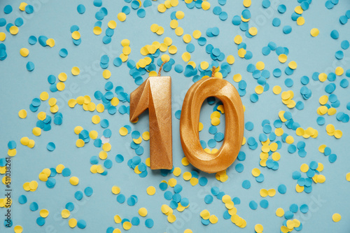 Number 10 ten golden celebration birthday candle on yellow and blue confetti Background. Ten years birthday. concept of celebrating birthday, anniversary, important date, holiday