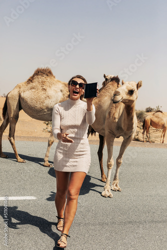 Photography A happy beautiful girl, smiling, takes a selfie with a camel by the road during
