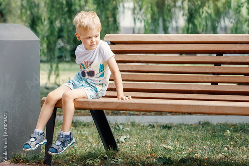 Small child plays in park. Kid is sitting on a park bench.