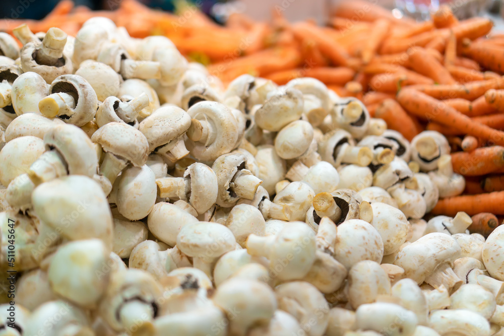 Close-up of fresh champignons on the counter in the store, fresh carrots in the background