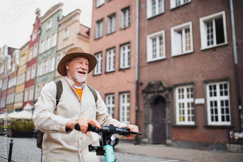 Portrait of happy senior man tourist riding scooter outdoors in town