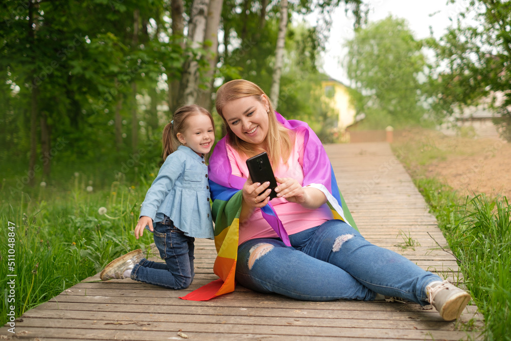 A mother with an LGBT flag and her little daughter take selfies on their smartphone. Funny girl and her mom. A mother with an LGBT flag and her little daughter take selfies on their smartphone. Funny girl and her mom.