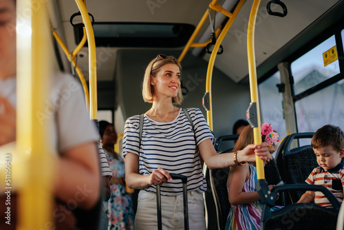 Group of people commuting by bus. The focus is on the young woman with suitcase holding the railing. photo