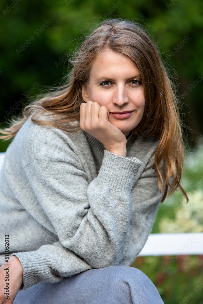 blond woman sitting outdoors in park on white bench blond woman sitting outdoors in park on white bench