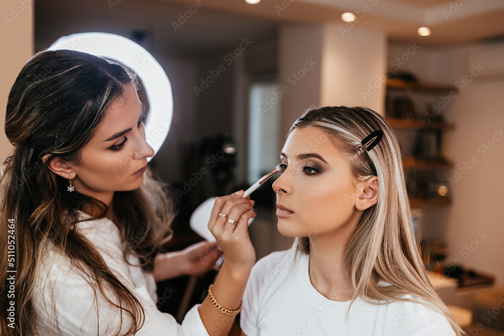 Close up shot of beautiful young woman face getting make-up. The artist is applying eyeshadow base with brush. Professional beautician work. Close up shot of beautiful young woman face getting make-up. The artist is applying eyeshadow base with brush. Professional beautician work.