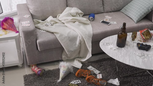 view of messy living room after a riotous drinking party. disorder, chaotic interior with beer bottles, shoes, cards scattered all over the room. decadent lifestyle concept