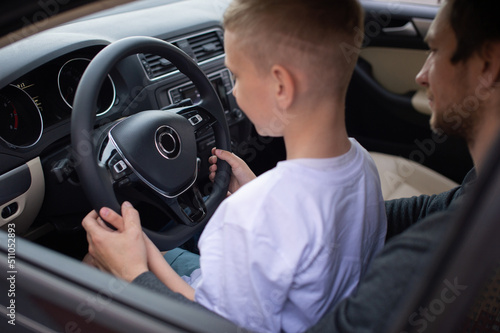 Dad and a cute boy hold the steering wheel of a car with their hands © Julia Jones