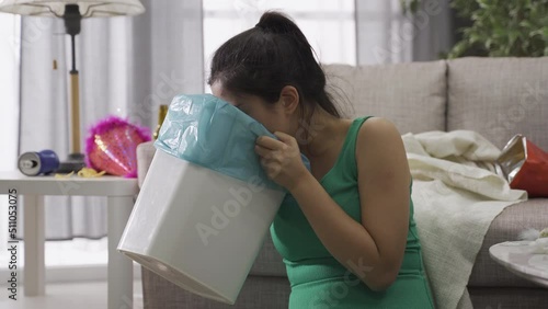 asian female with rubbish bin drinking an excess of alcohol feels terribly sick in the morning. taiwanese girl wiping her mouth feeling miserable after throwing up violently photo