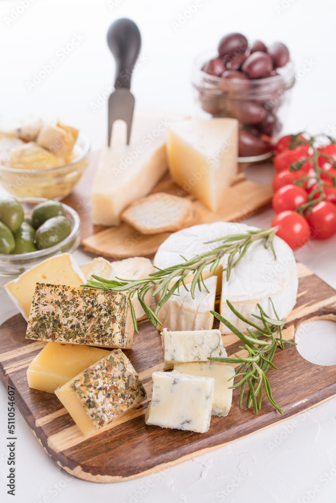 Cheese board with selection of cheeses served with olives, tomatoes and herbs on white table background. Cheese plate for aperitif - brie, dorblu, gorgonzola, camembert and parmesan Cheese board with selection of cheeses served with olives, tomatoes and herbs on white table background. Cheese plate for aperitif - brie, dorblu, gorgonzola, camembert and parmesan