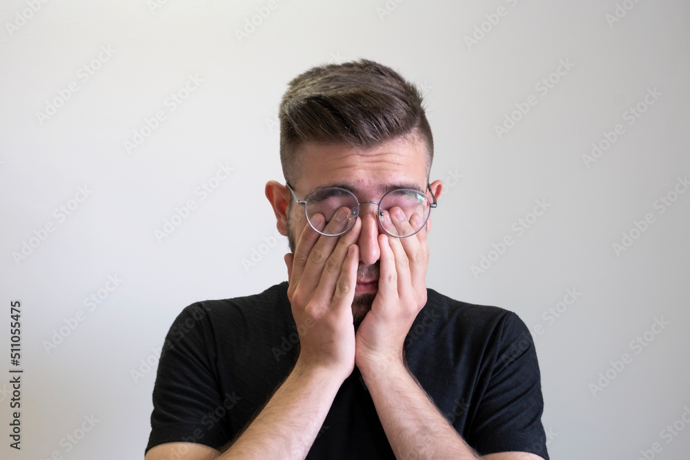 Young man rubbing his eyes, portrait of tired young man rubbing his eyes isolated on grey background. Caucasian, brown haired teenage boy wearing glasses. Young man rubbing his eyes, portrait of tired young man rubbing his eyes isolated on grey background. Caucasian, brown haired teenage boy wearing glasses.