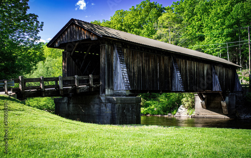 Bild auf Leinwand Weathered wooden country covered bridge  on a bright sunny day, trees and grass surrounding the bridge