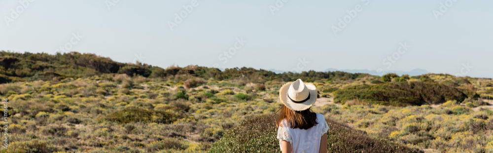 Back view of young woman in straw hat standing on beach with grass, banner.