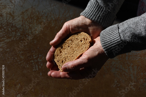 The hands of an elderly poor woman are holding a piece of bread. Concept of war, poverty, crisis and social inequality.