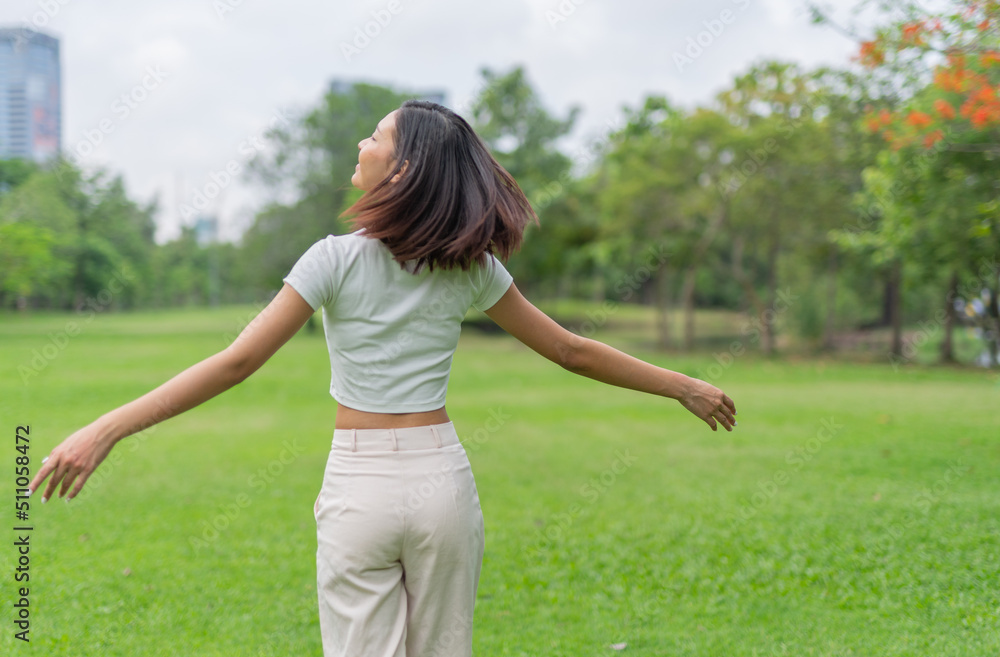 Portrait photo of a young beautiful asian female lady in white top embracing the breeze wind relaxingly and chillingly in a public park